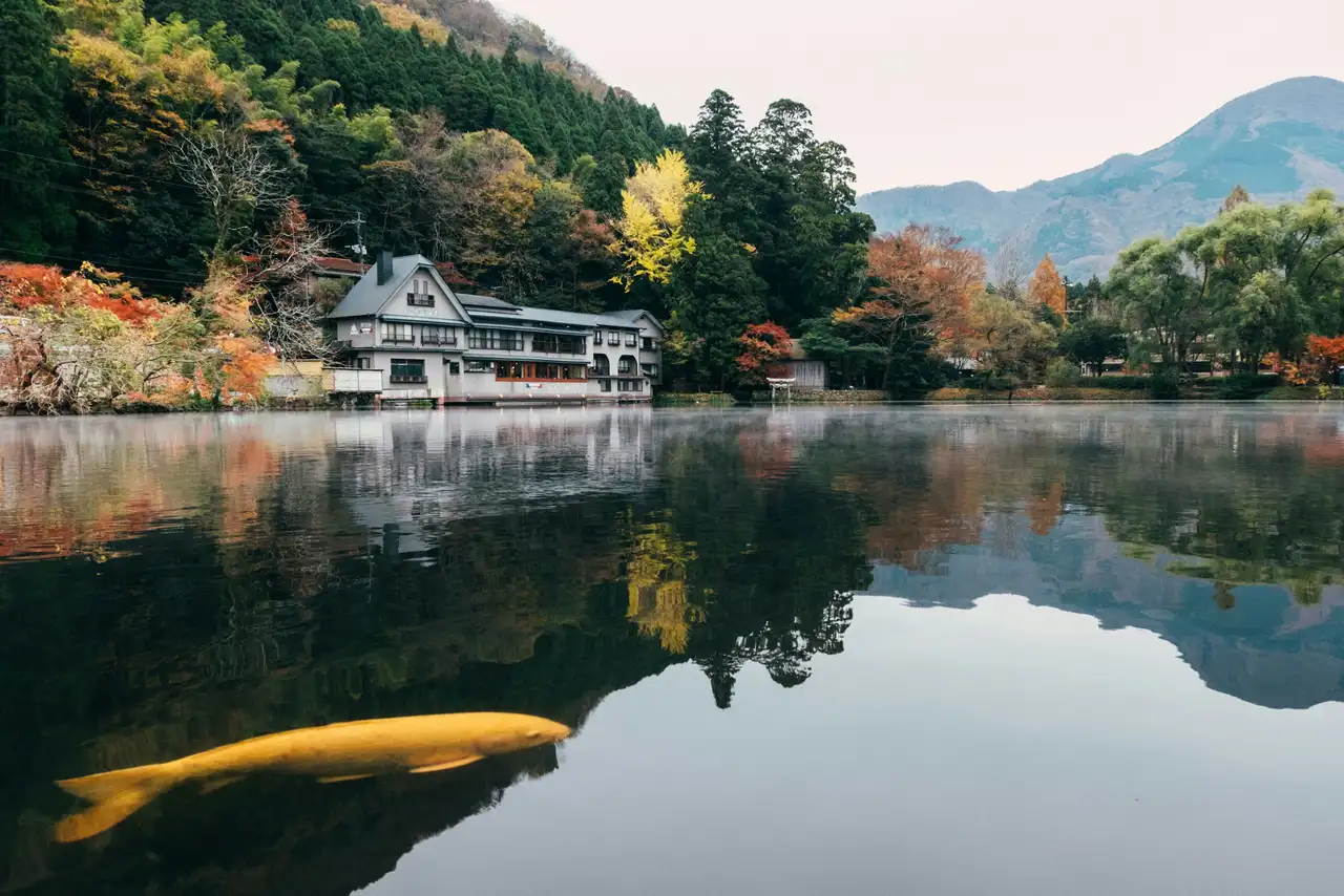 traditional japanese house reflecting on the calm waters of lake kinrin surrounded by autumn trees and mountains in yufuin kyushu