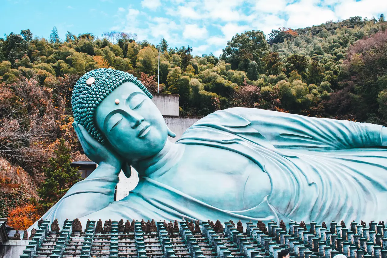 massive bronze reclining buddha statue surrounded by green trees and forest hills at nanzoin temple in kyushu