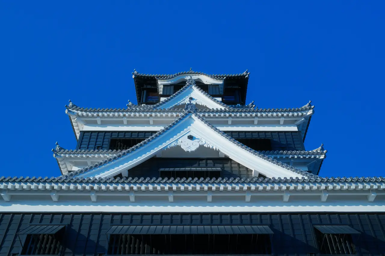 majestic white and black traditional rooftop architecture of the historic kumamoto castle against a clear blue sky in kyushu