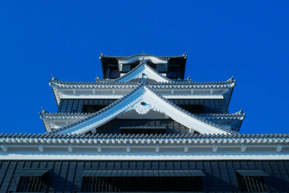 majestic white and black traditional rooftop architecture of the historic kumamoto castle against a clear blue sky in kyushu