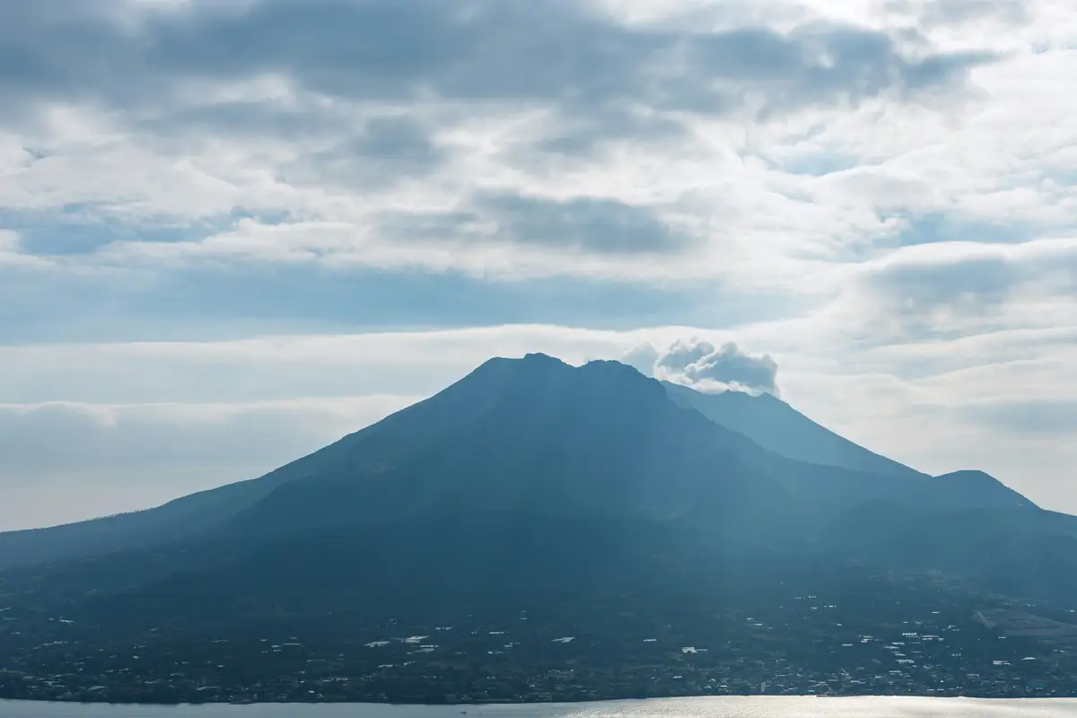 panoramic view of the active mount sakurajima volcano emitting light smoke over the bay under a cloudy sky in kagoshima kyushu