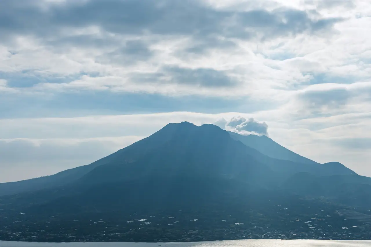 panoramic view of the active mount sakurajima volcano emitting light smoke over the bay under a cloudy sky in kagoshima kyushu