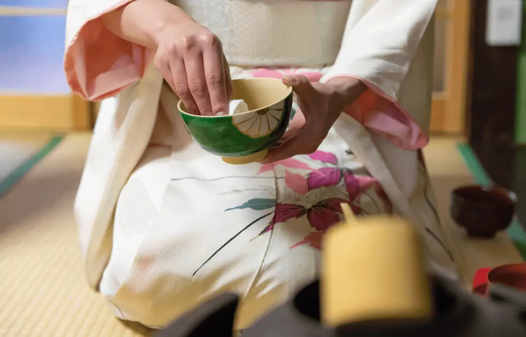 Route du thé au Japon – Femme en kimono nettoyant un bol à thé chawan vert et beige pendant la cérémonie du thé.