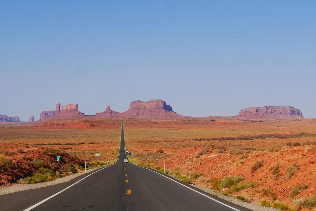 Longue route rectiligne traversant Monument Valley, avec des formations rocheuses rouges