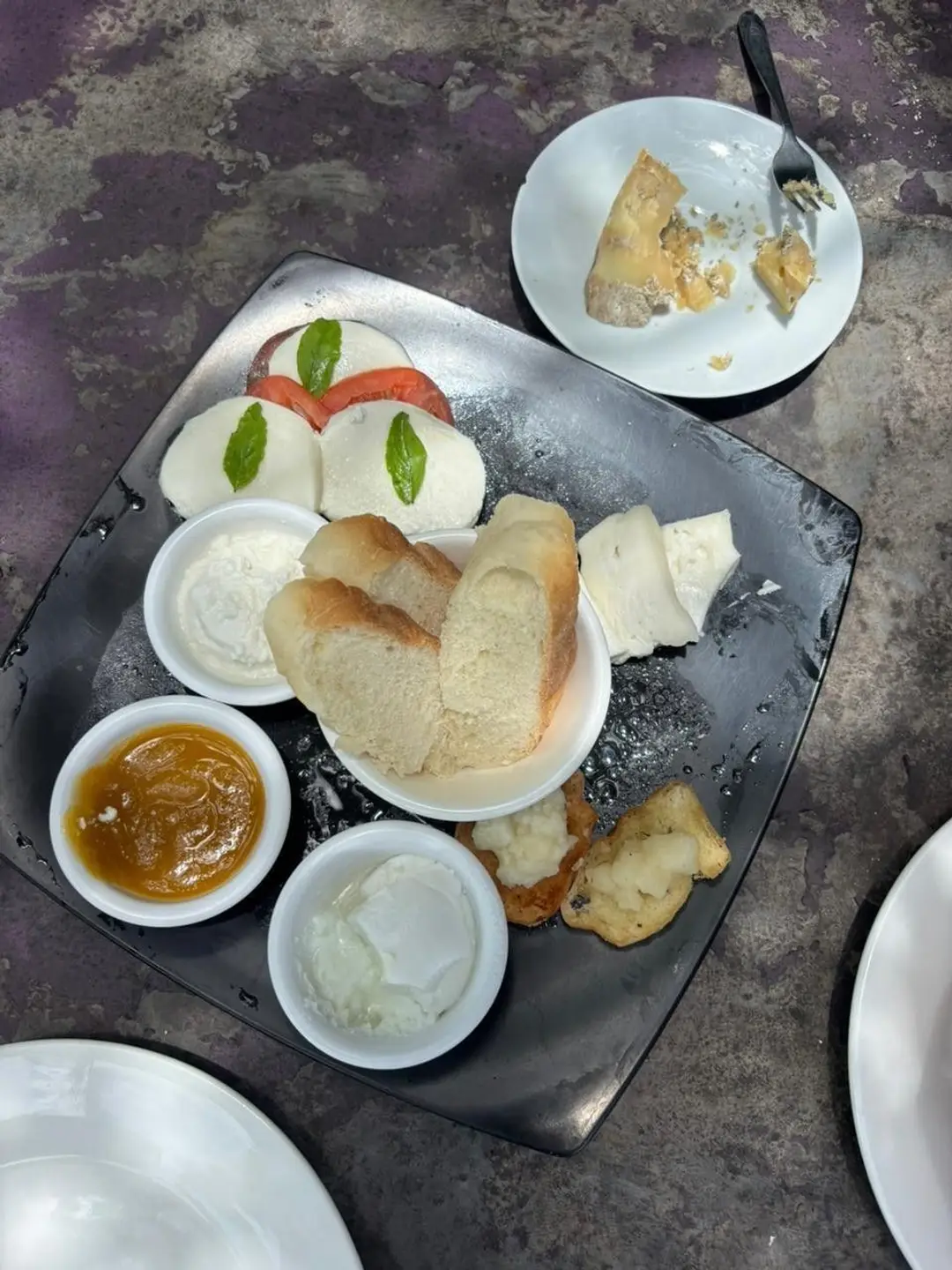 Une assiette de dégustation de produits laitiers artisanaux comprenant de la mozzarella fraîche aux tomates, du pain, du fromage blanc et des confitures.