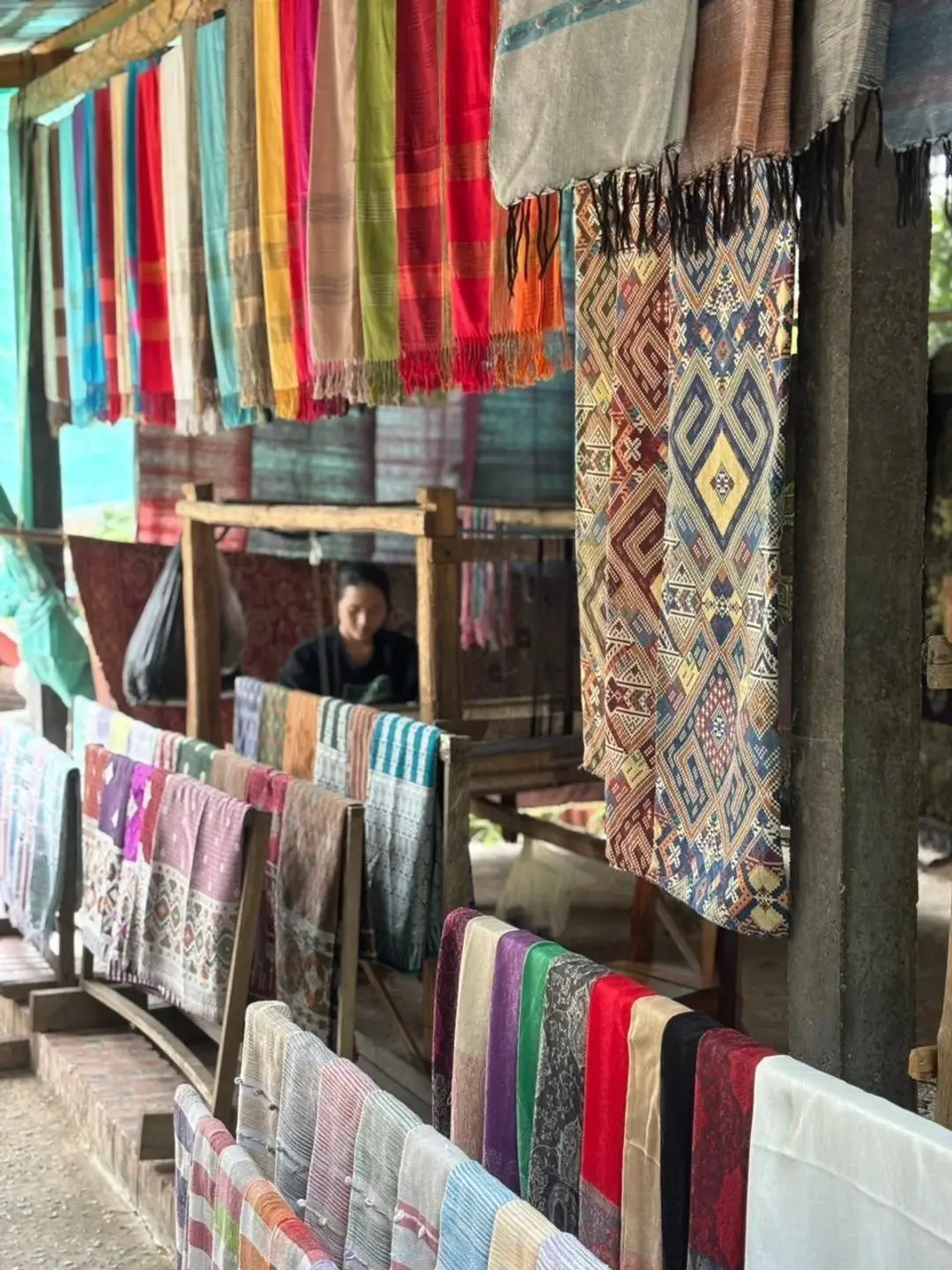 De nombreux foulards et tissus en soie colorés aux motifs traditionnels suspendus et exposés dans un atelier de tissage artisanal au Laos.