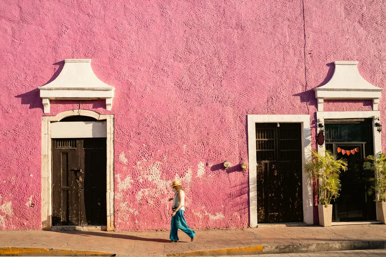 Une femme qui marche devant une maison rose à Izamal lors d'un voyage au Mexique