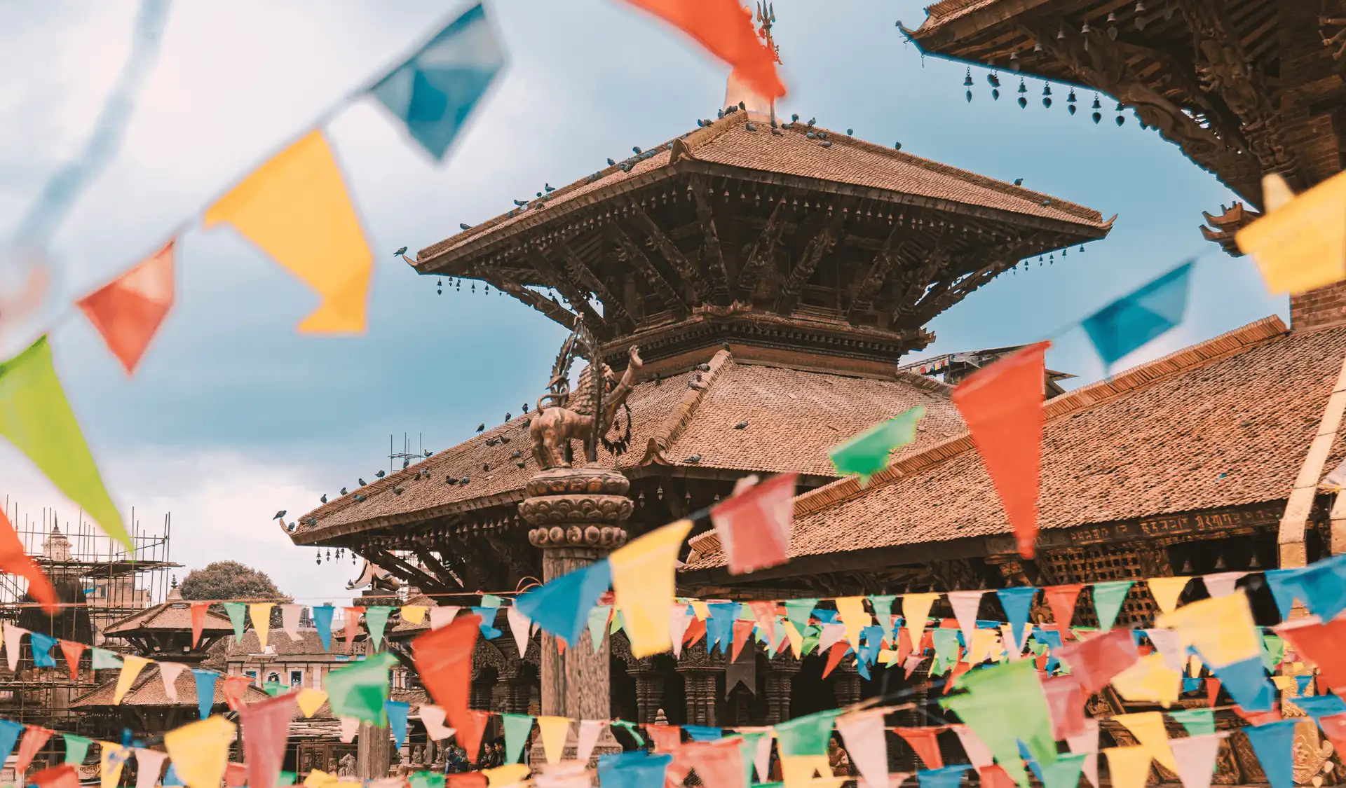 Architecture en bois traditionnelle du temple de Nyatapola à Bhaktapur au Népal, décorée de guirlandes de drapeaux de prières colorés sous un ciel lumineux.