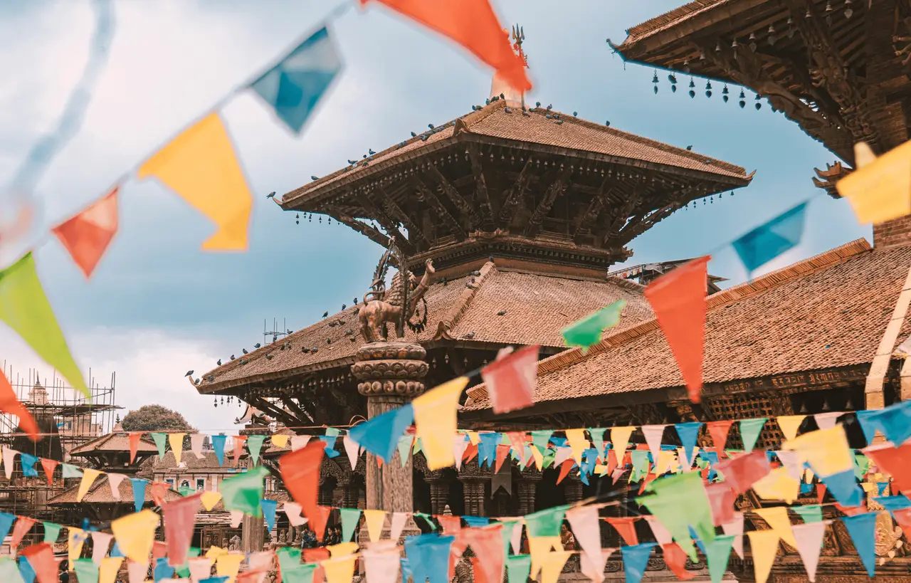 Architecture en bois traditionnelle du temple de Nyatapola à Bhaktapur au Népal, décorée de guirlandes de drapeaux de prières colorés sous un ciel lumineux.