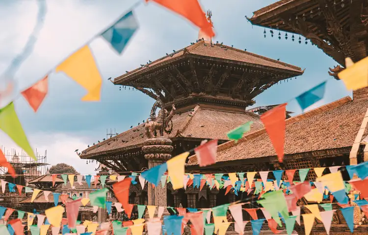 Architecture en bois traditionnelle du temple de Nyatapola à Bhaktapur au Népal, décorée de guirlandes de drapeaux de prières colorés sous un ciel lumineux.