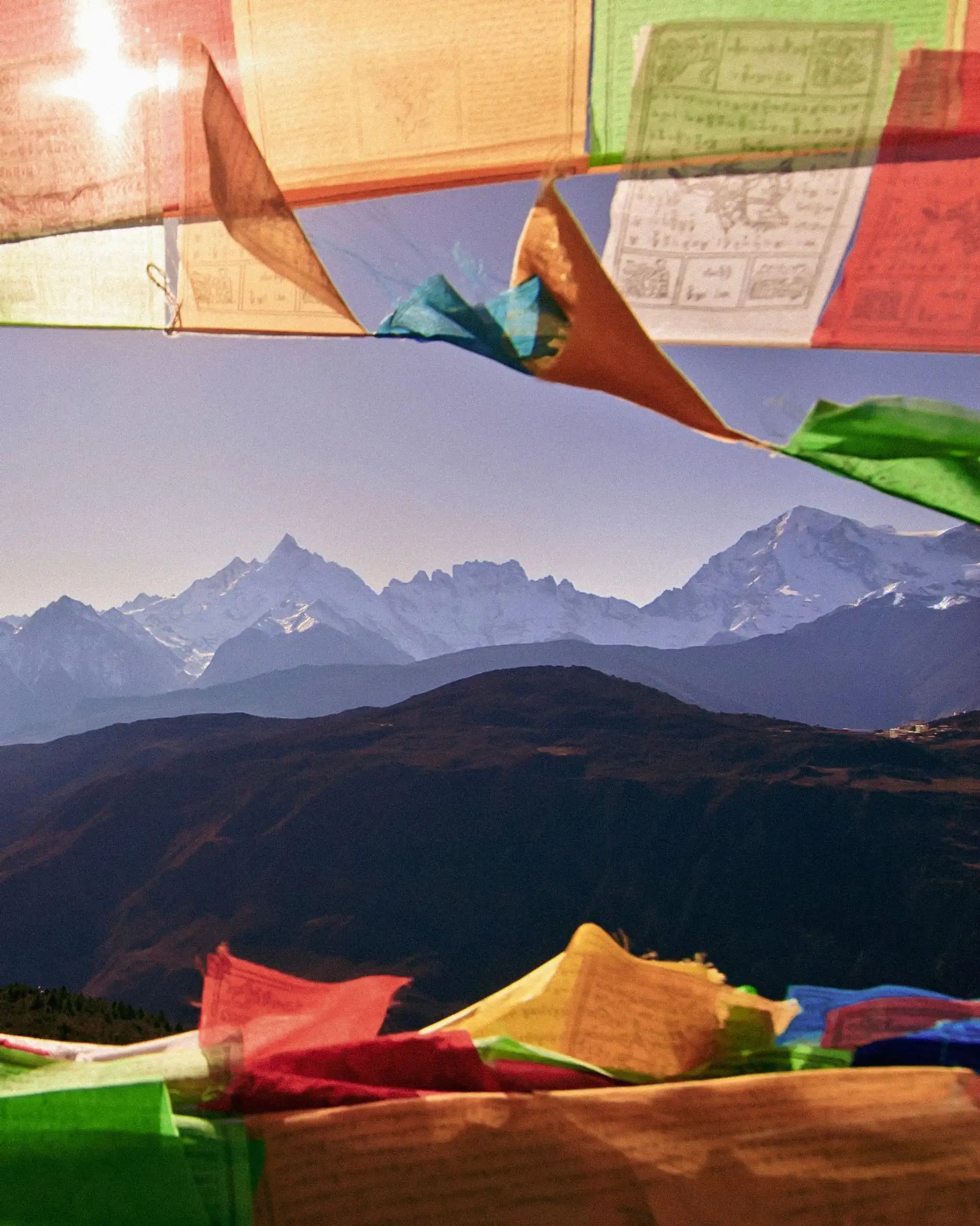 Drapeaux de prières tibétains colorés flottant au vent au premier plan, avec une vue lointaine sur la chaîne de montagnes enneigée de l'Himalaya au Népal.