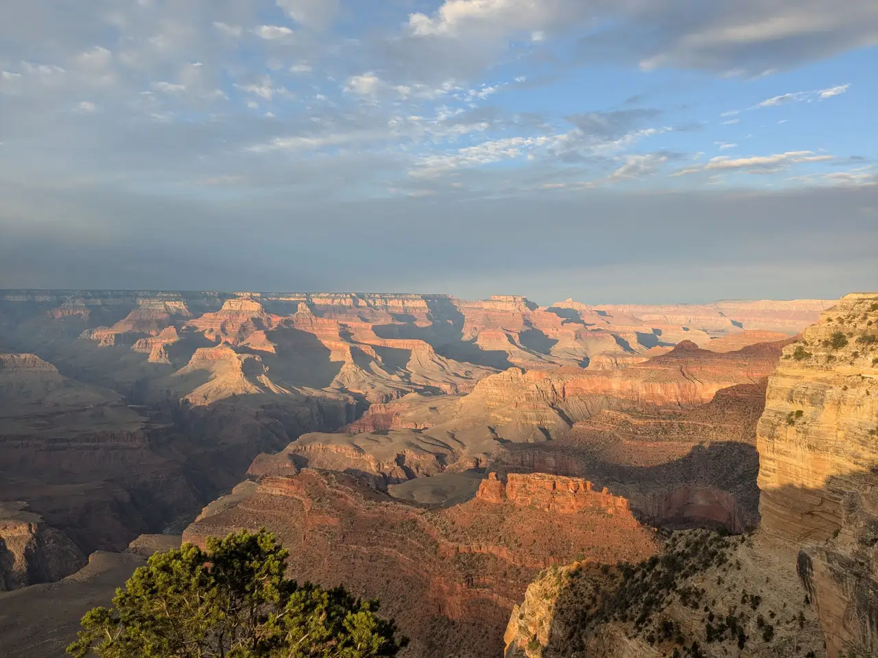 Vue panoramique sur les falaises rocheuses ocres et les failles du Grand Canyon sous un ciel nuageux en fin de journée