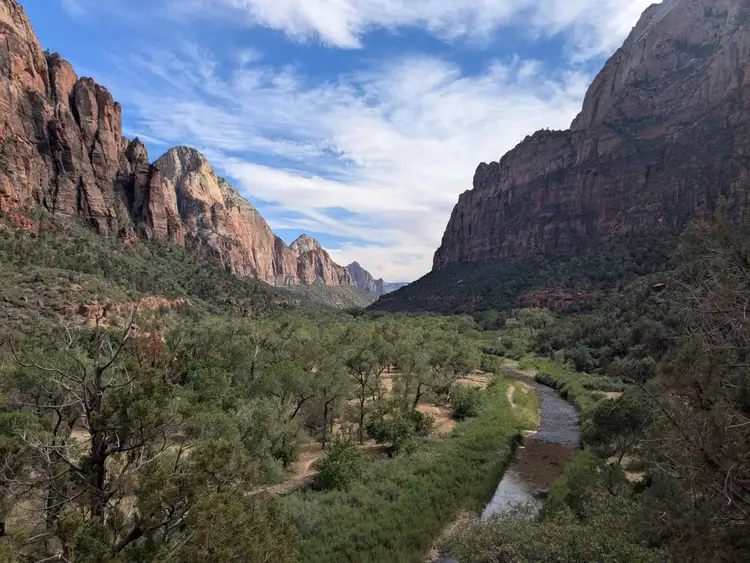 Vue sur la vallée verdoyante et la rivière encadrées par les vertigineuses falaises de grès rouge du parc national de Zion sous un ciel nuageux
