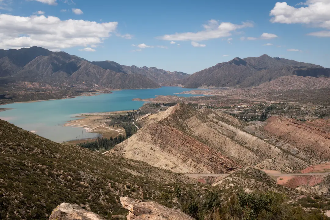 Paysage pittoresque des Andes avec un lac serein et des collines vallonnées sous un ciel bleu éclatant.
