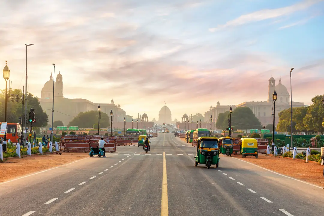 De nombreux tuk-tuks verts et jaunes circulant sur la grande avenue menant au palais présidentiel du Rashtrapati Bhavan sous un ciel de lever de soleil à New Delhi en Inde.