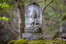 Une ancienne statue de Bouddha en pierre sculptée, moussue et entourée par la végétation forestière sacrée du temple Risshakuji à Yamadera au Japon.