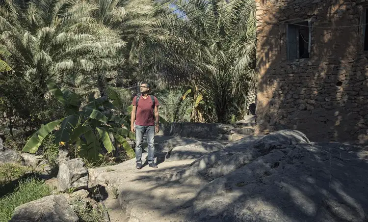 Voyage à Oman — Un randonneur explorant les sentiers pierreux du vieux village d'Al Hamra entouré de palmiers.