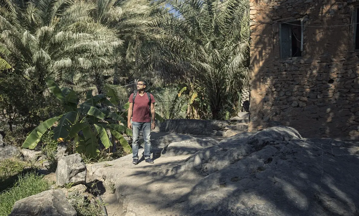 Voyage à Oman — Un randonneur explorant les sentiers pierreux du vieux village d'Al Hamra entouré de palmiers.