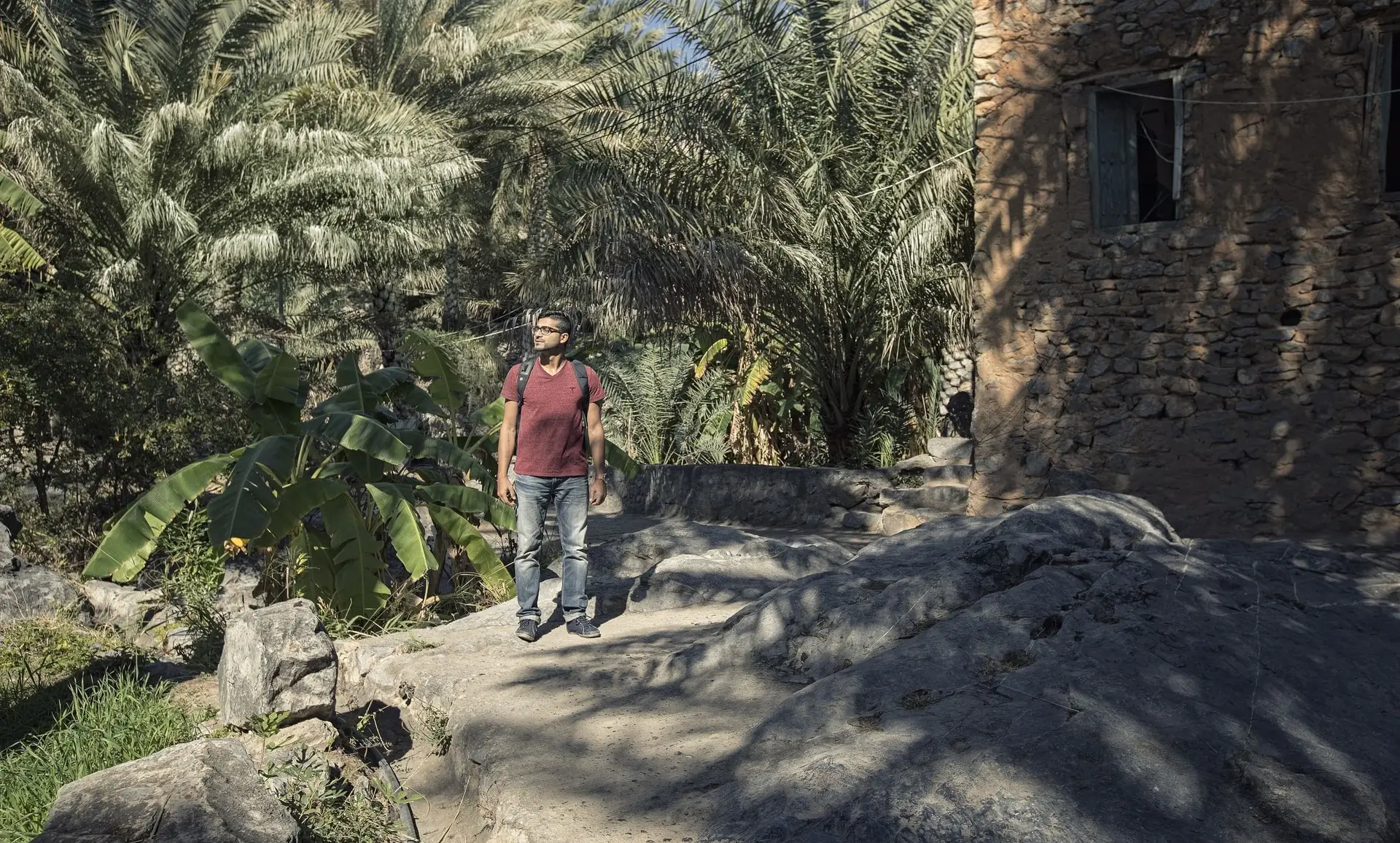 Voyage à Oman — Un randonneur explorant les sentiers pierreux du vieux village d'Al Hamra entouré de palmiers.