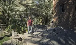 Voyage à Oman — Un randonneur explorant les sentiers pierreux du vieux village d'Al Hamra entouré de palmiers.