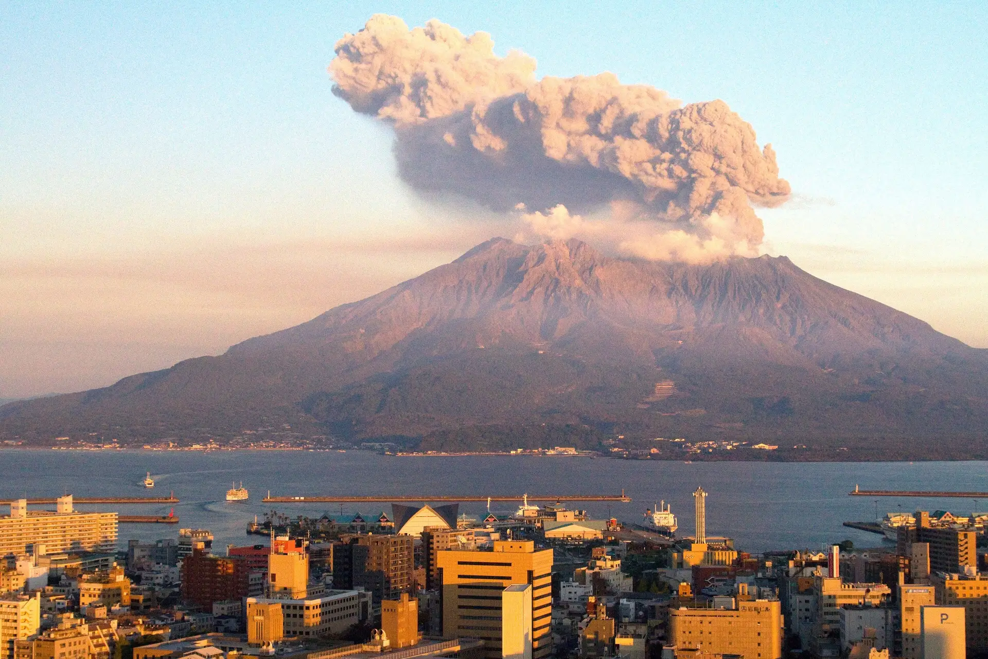 Voyage au Japon – Vue panoramique sur le volcan Sakurajima en activité surplombant la ville de Kagoshima au coucher du soleil.