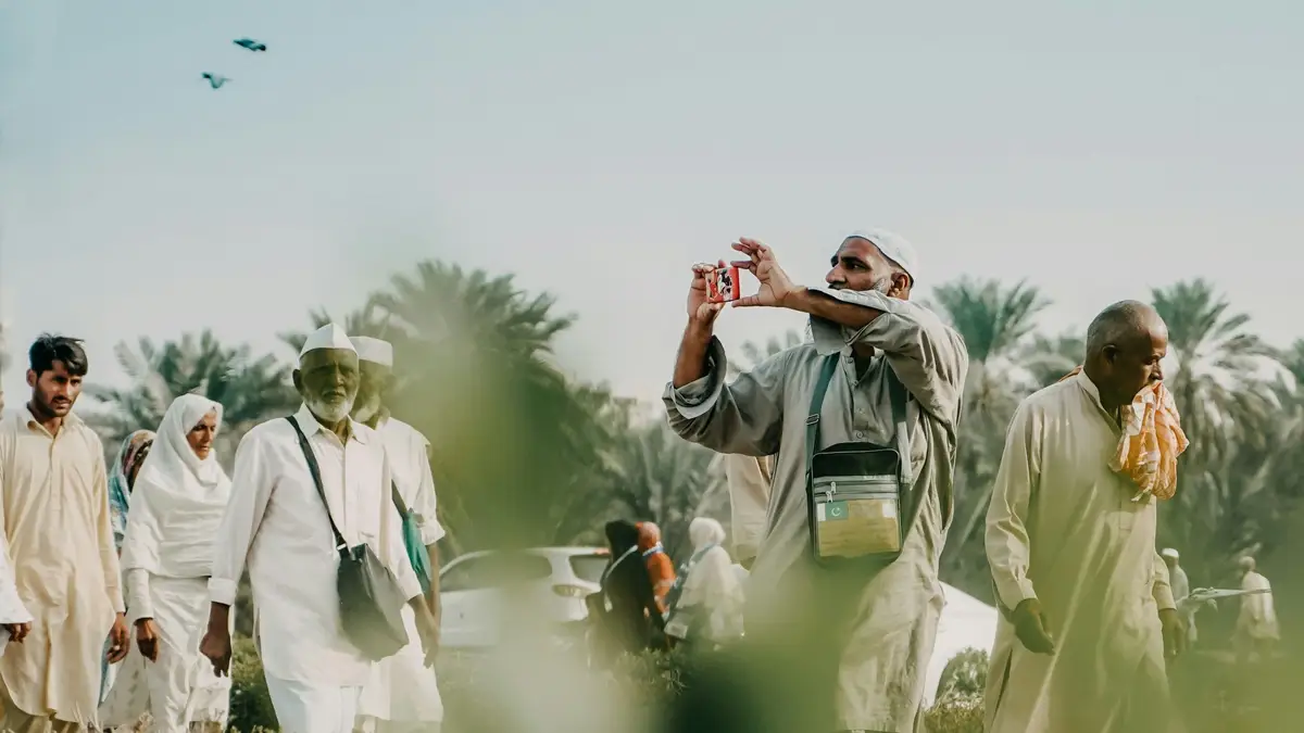 Homme en tenue traditionnelle prenant une photo dans une palmeraie en Arabie Saoudite.