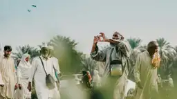 Homme en tenue traditionnelle prenant une photo dans une palmeraie en Arabie Saoudite.