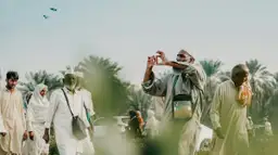 Homme en tenue traditionnelle prenant une photo dans une palmeraie en Arabie Saoudite.