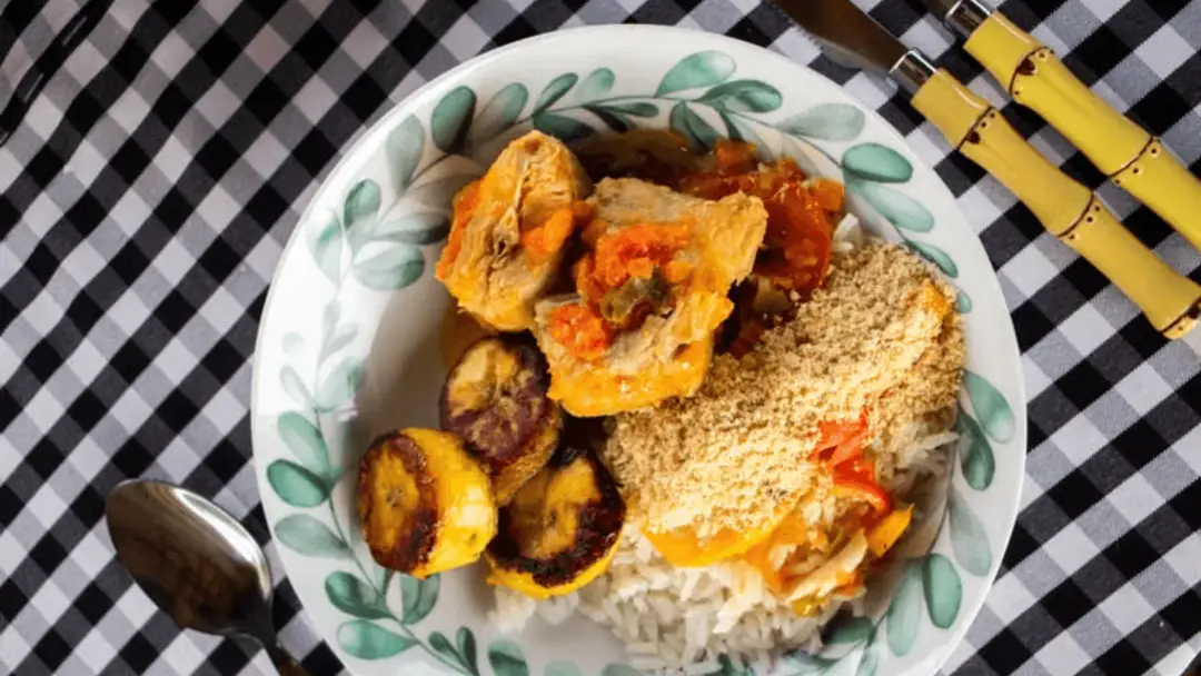 Repas brésilien composé de riz, de poulet, de bananes plantain frites et de farofa.