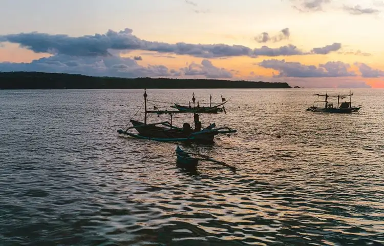 Voyage en Asie — Un jukung traditionnel naviguant au lever du soleil sur les eaux calmes de Bali.