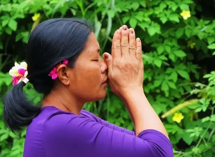 Voyage en Asie — Gros plan d'une femme balinaise en prière à Bali : geste de dévotion avec fond de feuillage tropical flou.