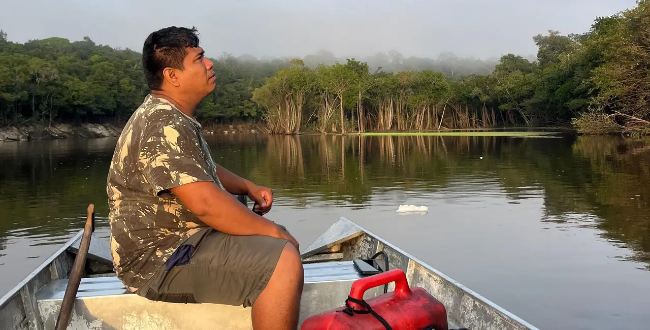 Voyage au Brésil – Un homme navigue à bord d'une embarcation en bois traditionnelle sur un fleuve amazonien bordé par la forêt tropicale dense près de Manaus.