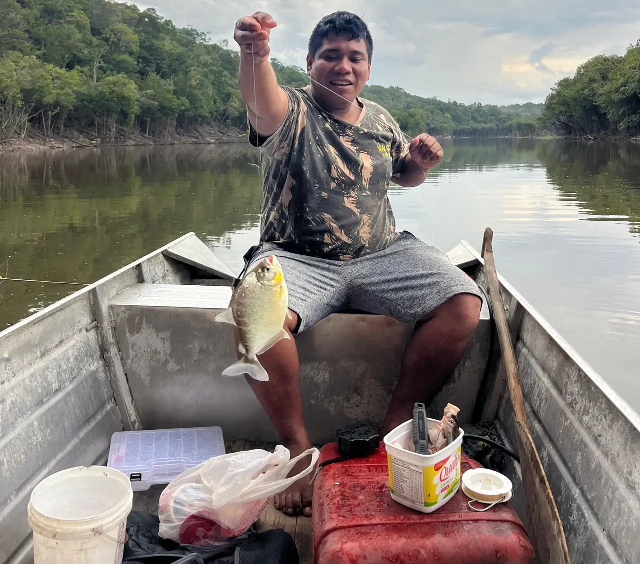 Voyage au Brésil – Un homme à bord d'un canoë montre fièrement un poisson piranha pêché dans les eaux d'un fleuve en Amazonie.