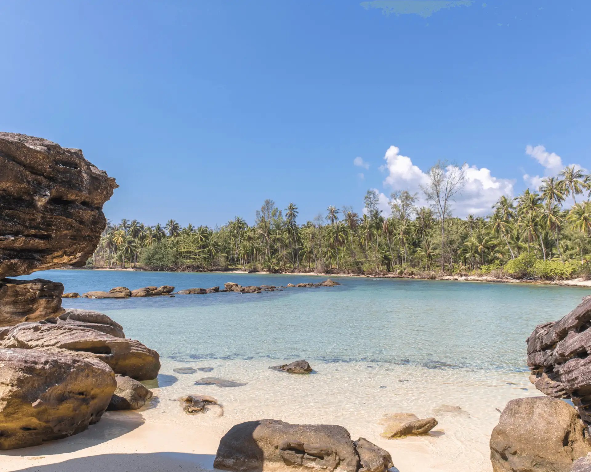 Plage sauvage de Koh Kood avec rochers sculptés, sable fin et eau transparente bordée de cocotiers.
