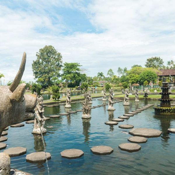 Voyage en Asie — Bassin et statues du palais aquatique Tirta Gangga à Bali : lumière vive et végétation tropicale luxuriante.