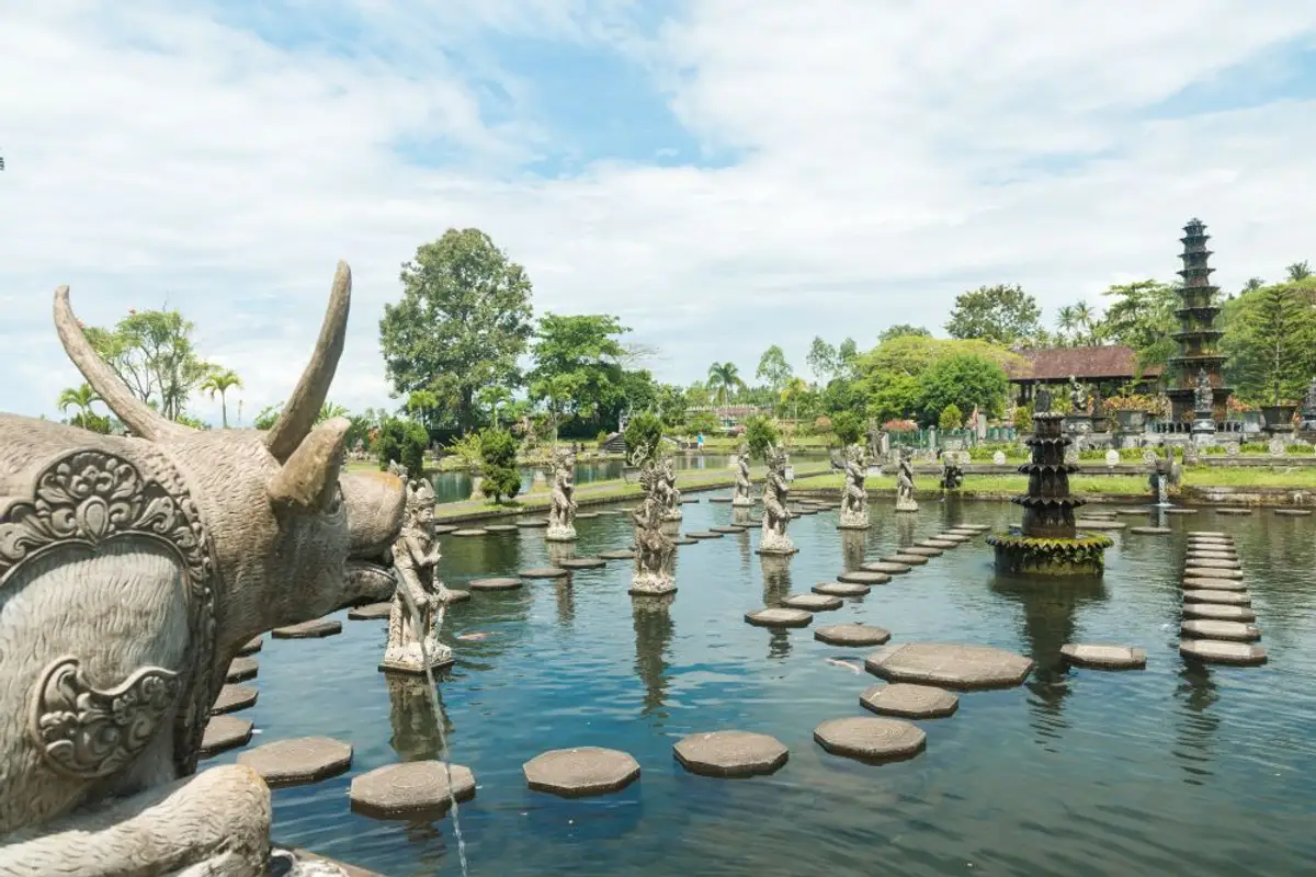 Voyage en Asie — Bassin et statues du palais aquatique Tirta Gangga à Bali : lumière vive et végétation tropicale luxuriante.