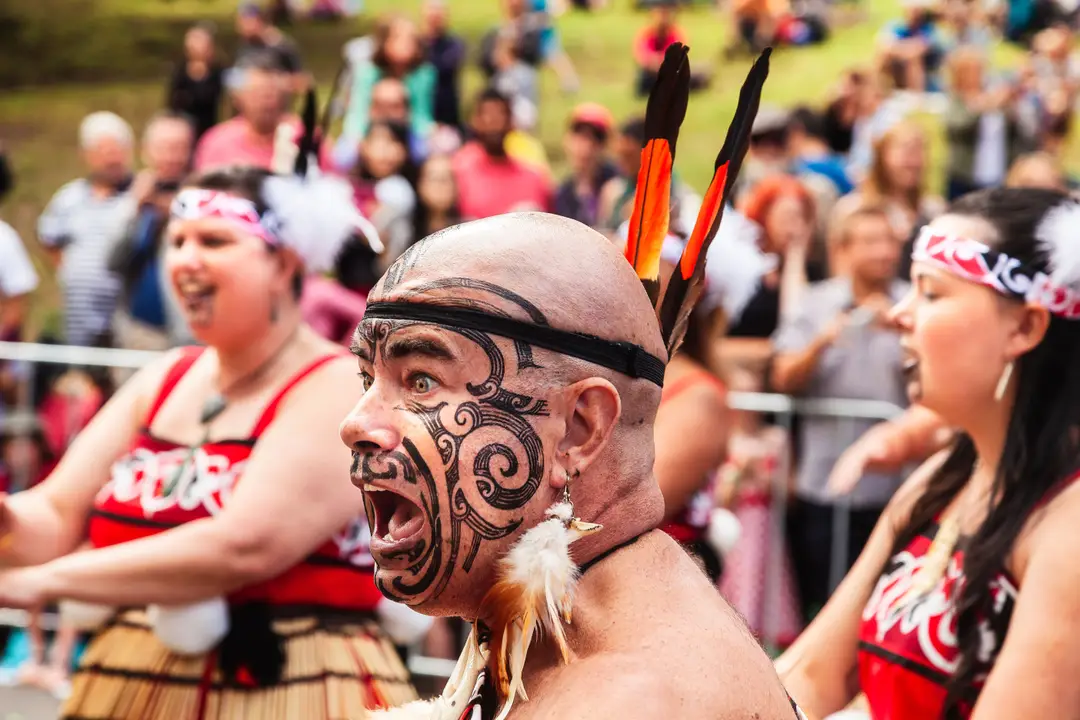 Un artiste māorie énergique avec un visage peint lors d'un festival tribal en plein jour