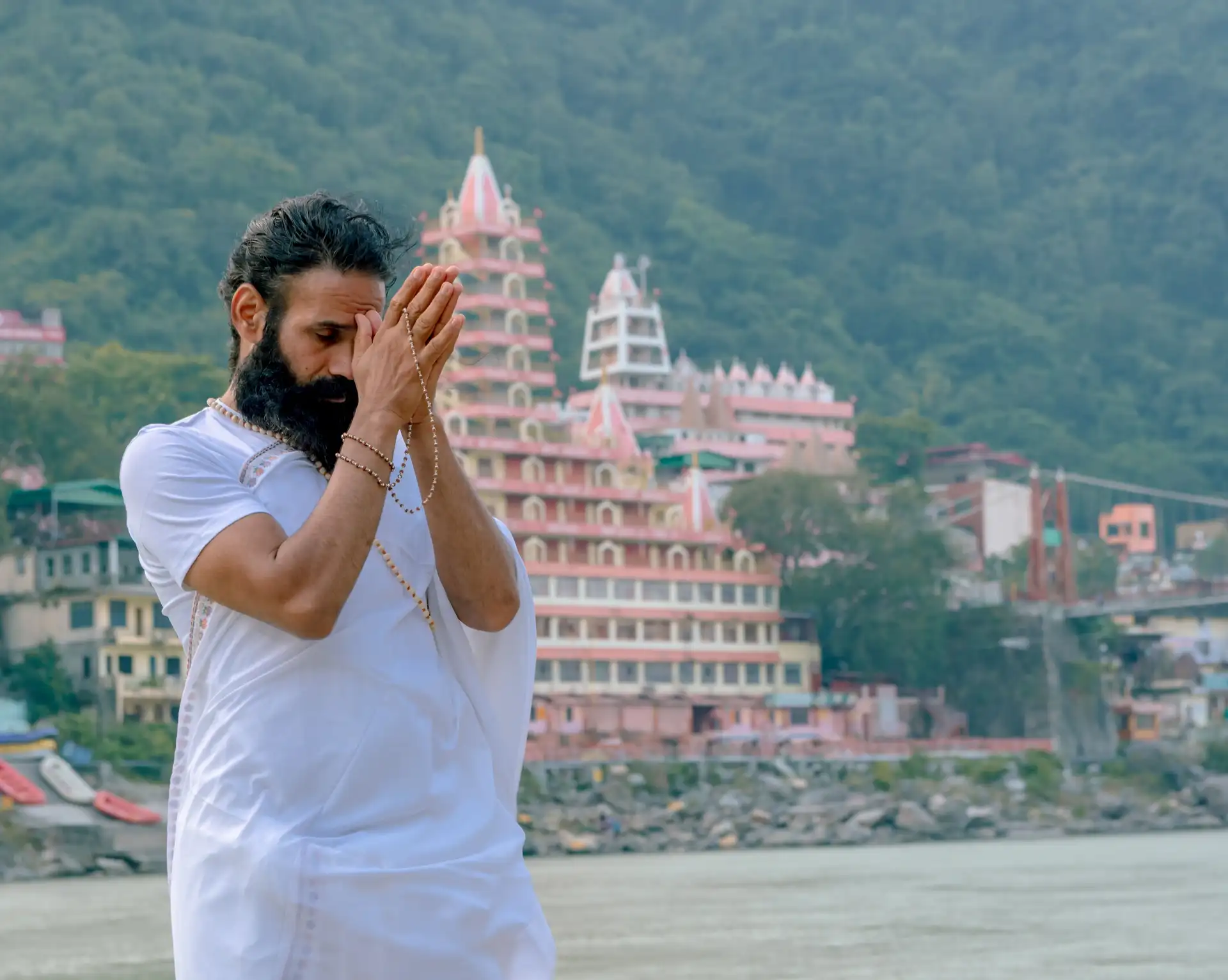 Homme en vêtements blancs priant en méditation sur les rives du Gange devant un temple à Rishikesh.