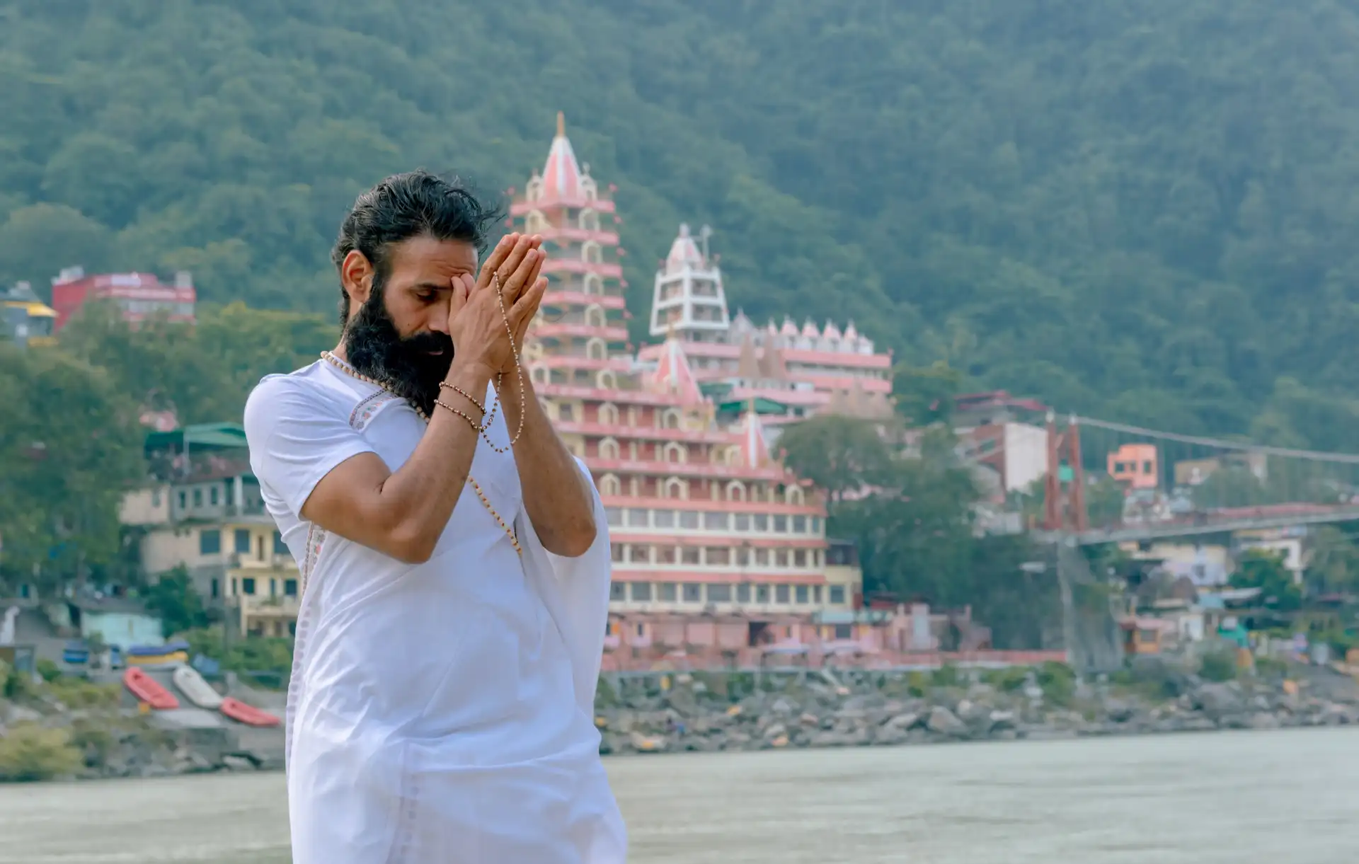 Homme en vêtements blancs priant en méditation sur les rives du Gange devant un temple à Rishikesh.