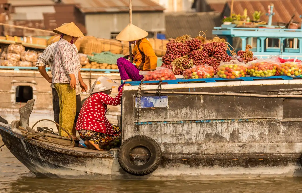 Des marchands locaux portant le chapeau conique traditionnel vietnamien s'activent sur des bateaux en bois remplis de fruits et de marchandises au marché flottant dans le delta du Mékong au Vietnam.
