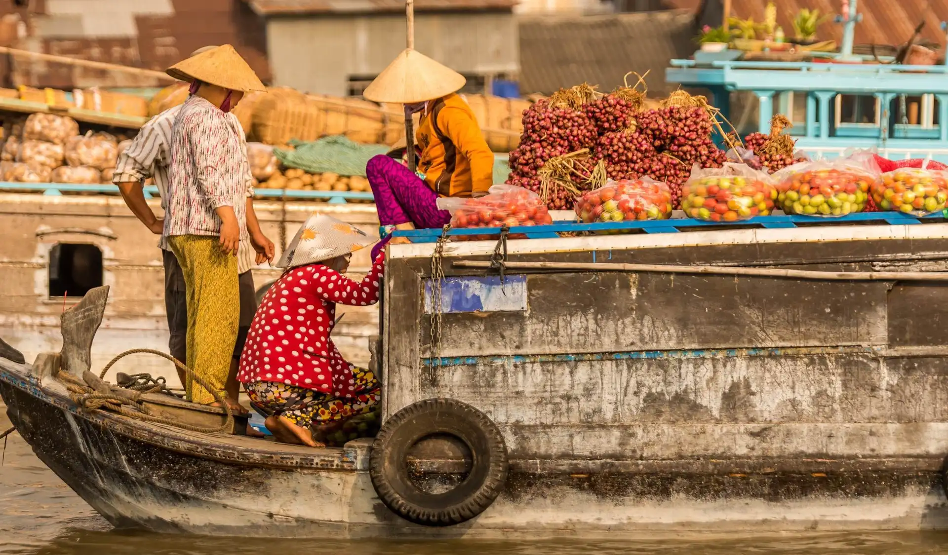 Des marchands locaux portant le chapeau conique traditionnel vietnamien s'activent sur des bateaux en bois remplis de fruits et de marchandises au marché flottant dans le delta du Mékong au Vietnam.