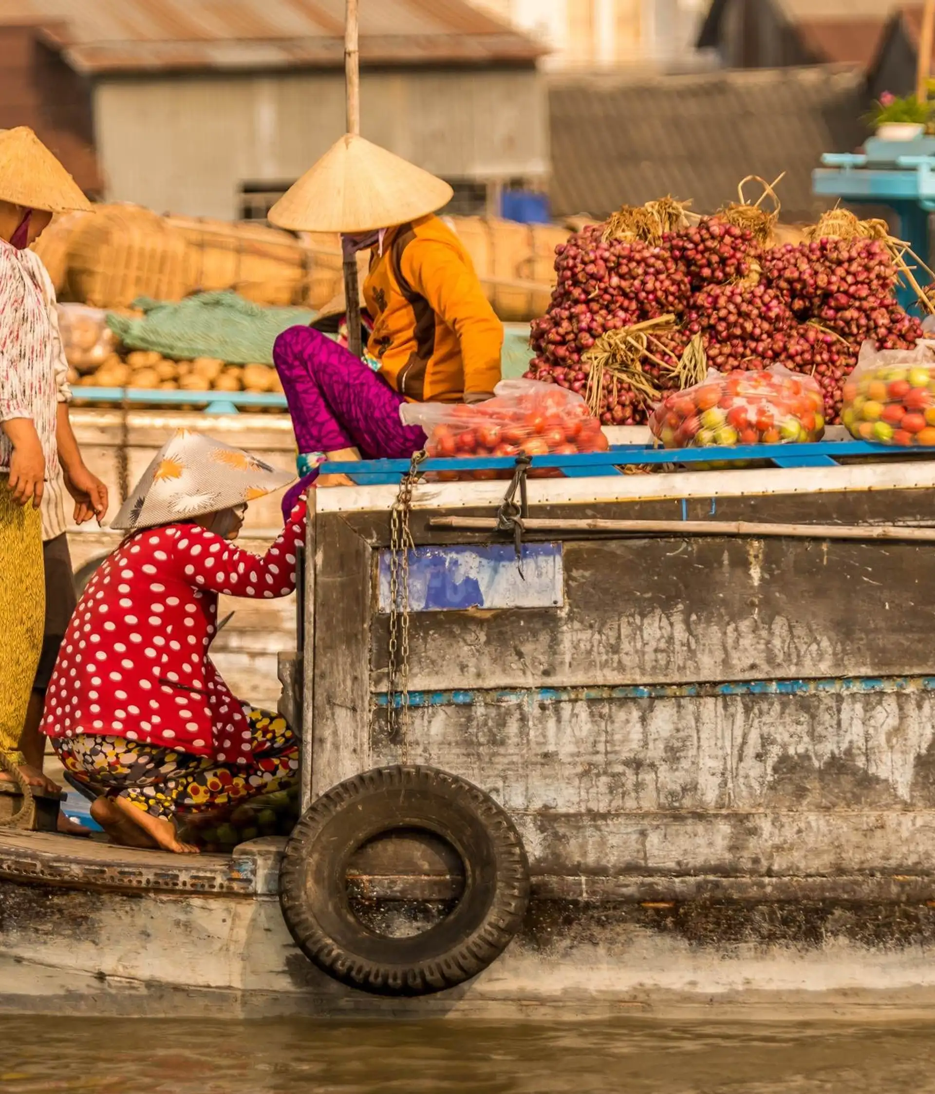 Des marchands locaux portant le chapeau conique traditionnel vietnamien s'activent sur des bateaux en bois remplis de fruits et de marchandises au marché flottant dans le delta du Mékong au Vietnam.