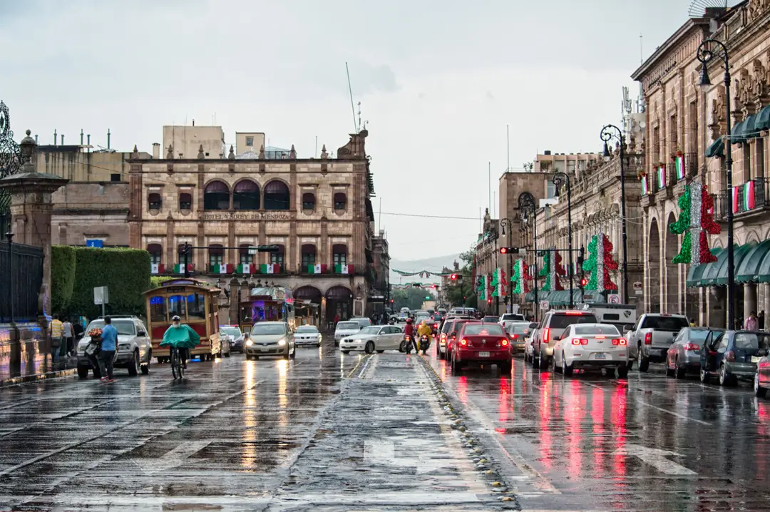 Rue animée d’une ville mexicaine sous la pluie, avec des voitures en circulation
