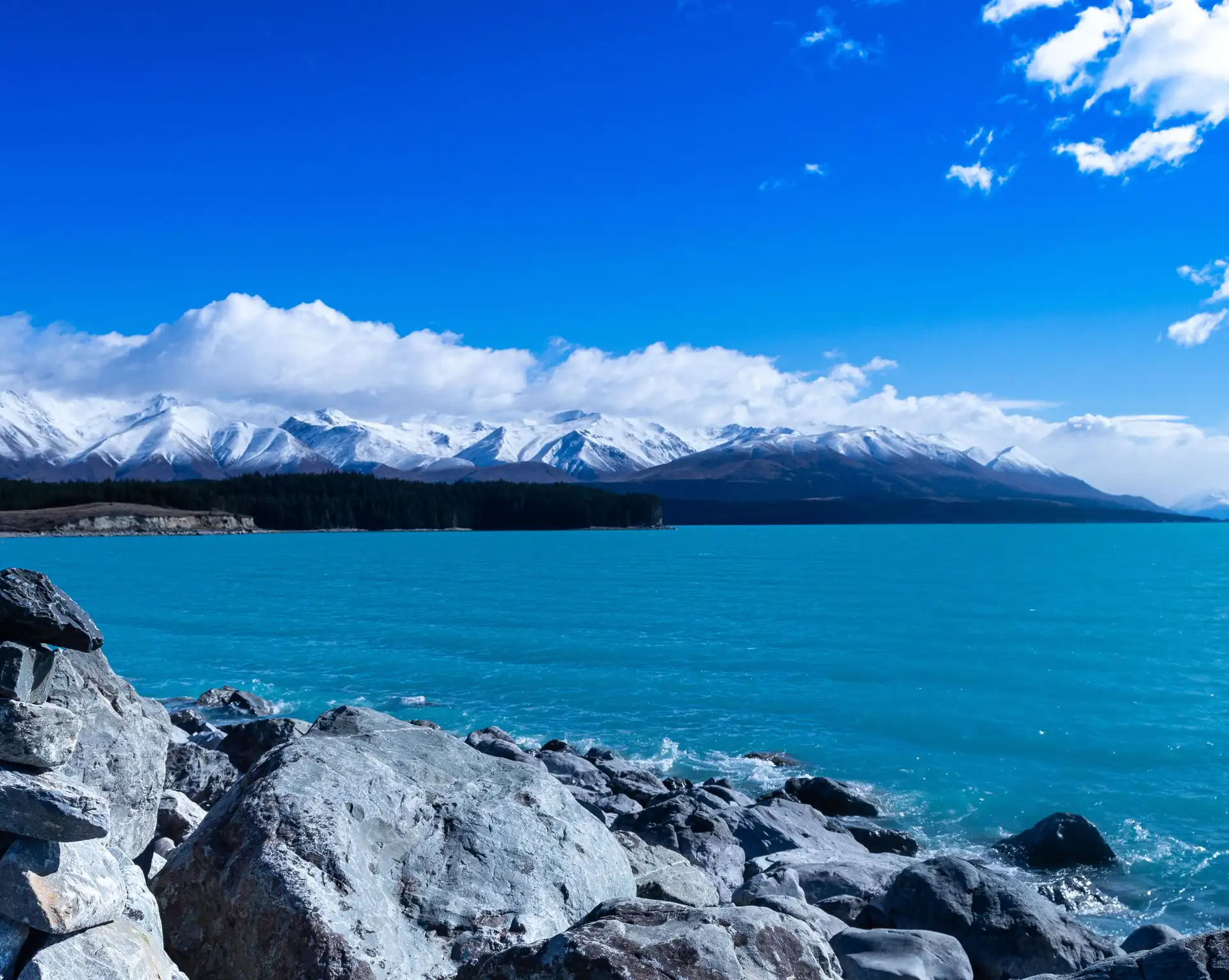 Vue panoramique sur les eaux bleues turquoises du lac Tekapo et la chaîne enneigée des Alpes du Sud en Nouvelle-Zélande.