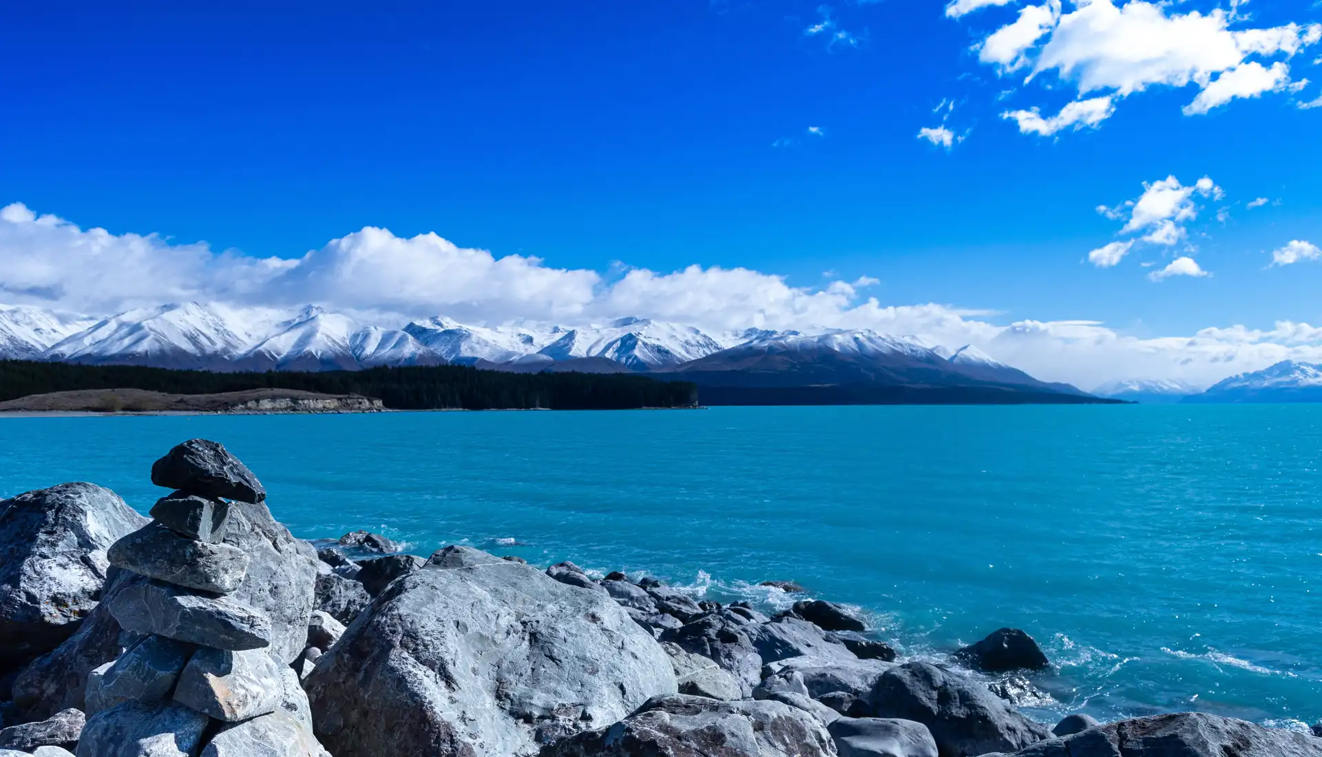 Vue panoramique sur les eaux bleues turquoises du lac Tekapo et la chaîne enneigée des Alpes du Sud en Nouvelle-Zélande.