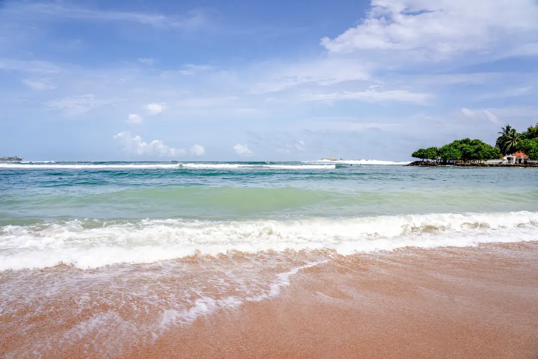 Vue sereine de la plage de Weligama avec des vagues frappant doucement le rivage sous un ciel clair.jpg