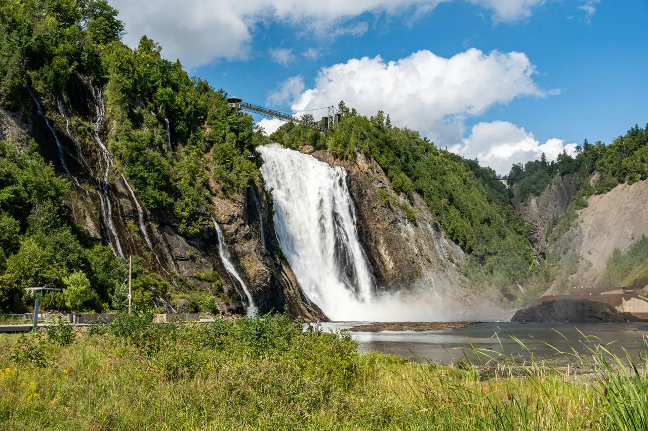 Impressionnante chute Montmorency s'écoulant le long d'une falaise rocheuse boisée sous une passerelle suspendue et un ciel d'été ensoleillé