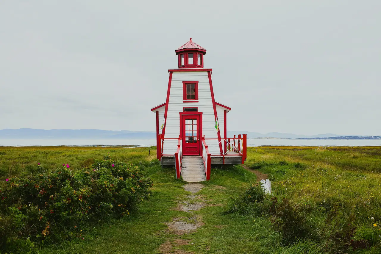 Phare en bois blanc et rouge bordé de végétation côtière devant les eaux calmes du fleuve Saint-Laurent à Rivière-du-Loup