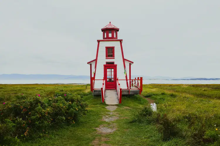 Phare en bois blanc et rouge bordé de végétation côtière devant les eaux calmes du fleuve Saint-Laurent à Rivière-du-Loup