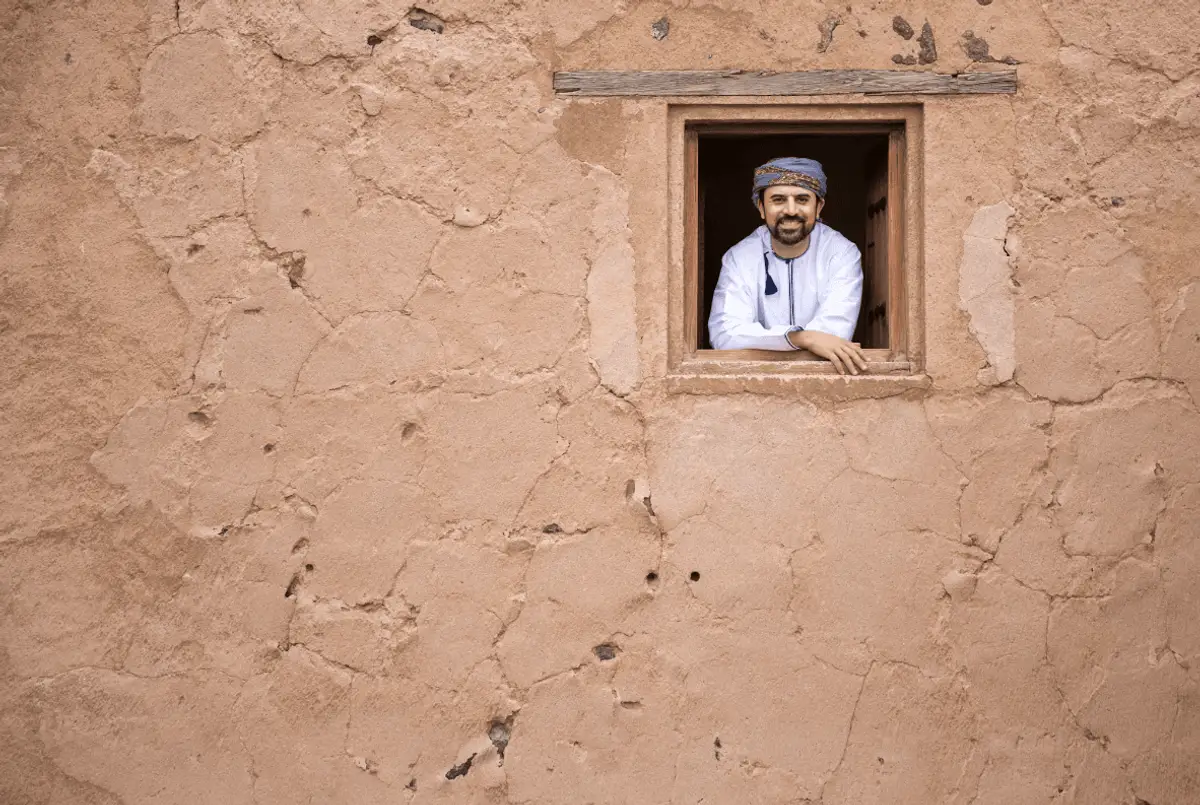 Homme omanais souriant à la fenêtre d'une maison traditionnelle en briques de terre à Oman
